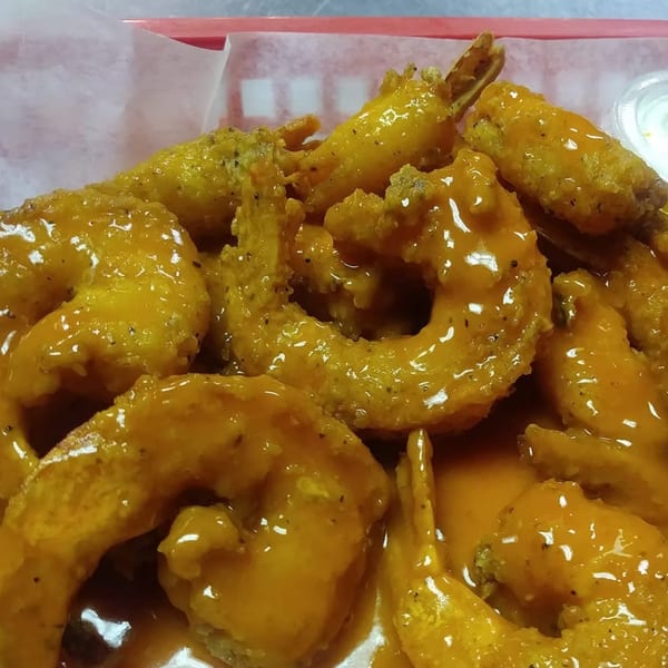 Close-up of golden-brown fried shrimp coated in a vibrant orange sauce, served in a red basket.