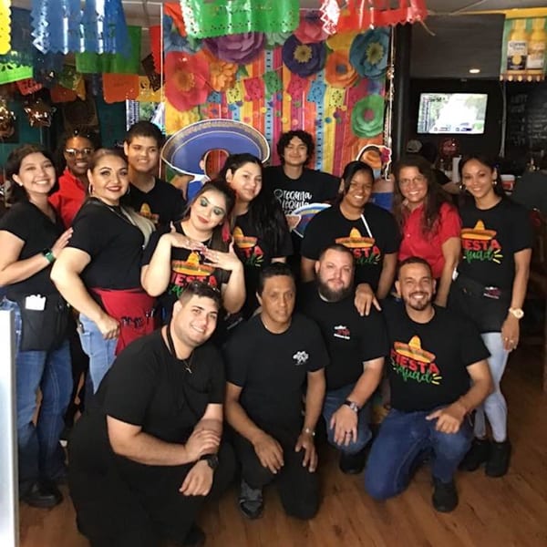 San Diego's Mexican Grill staff, a diverse group, smiling in front of colorful Mexican decorations.