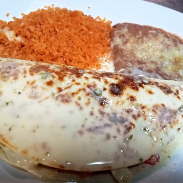 A San Diego's Mexican Grill burrito covered in white sauce, with orange rice and refried beans.