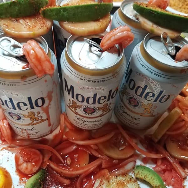 Modelo beer cans garnished with shrimp, avocado, and red onions in a spicy sauce.