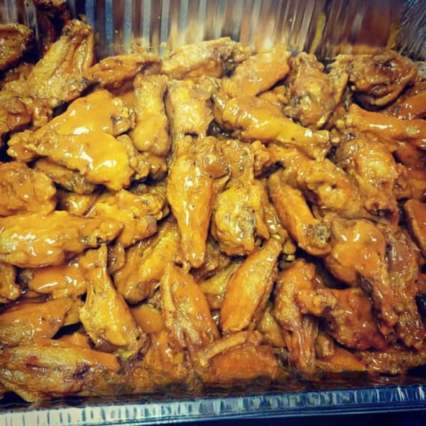 A large tray of golden-brown chicken wings coated in a rich, glossy sauce, ready to be served.