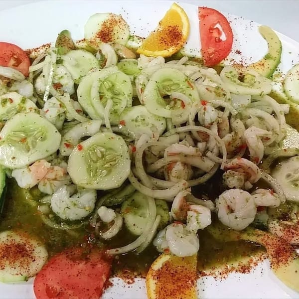 Mexican shrimp ceviche with cucumbers, onions, tomatoes, avocado, and orange slices on a white plate.