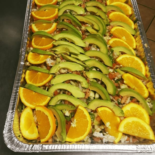 A catering tray of ceviche topped with alternating slices of fresh orange and avocado.