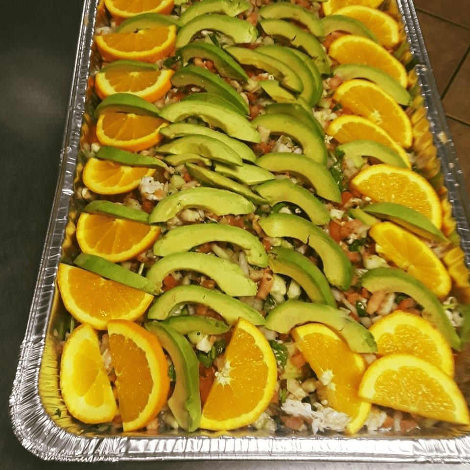 A catering tray of ceviche topped with alternating slices of fresh orange and avocado.
