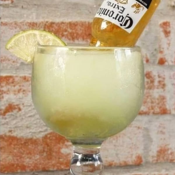 A large frozen margarita with a lime wedge and an upside-down Corona beer bottle in it.