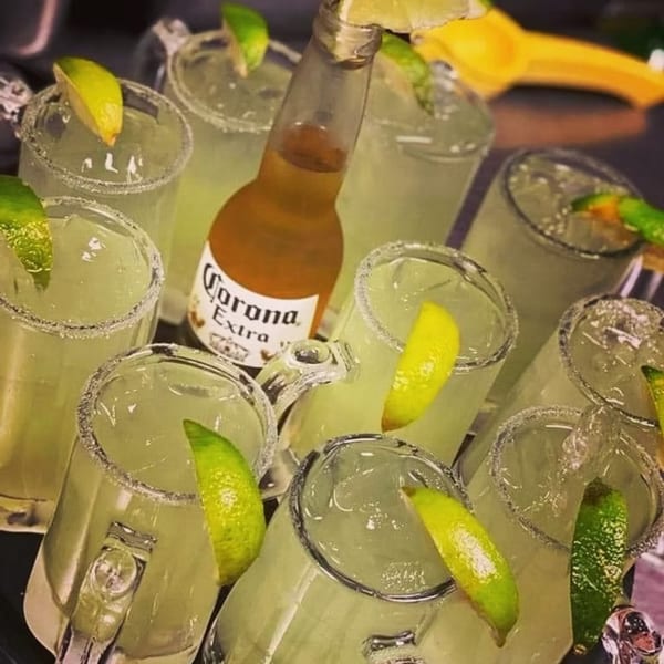 A tray of margaritas with lime wedges and a Corona Extra beer bottle.